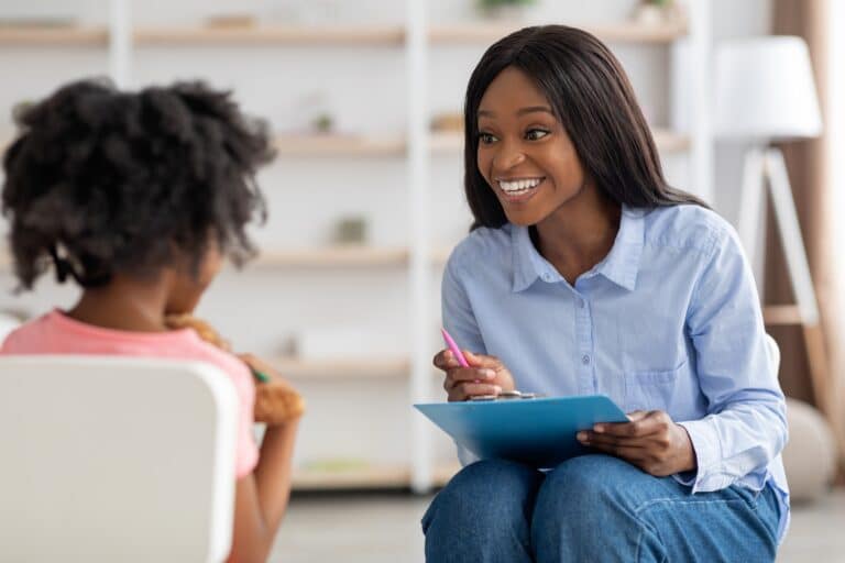 Smiling pretty black woman child development specialist talking to girl